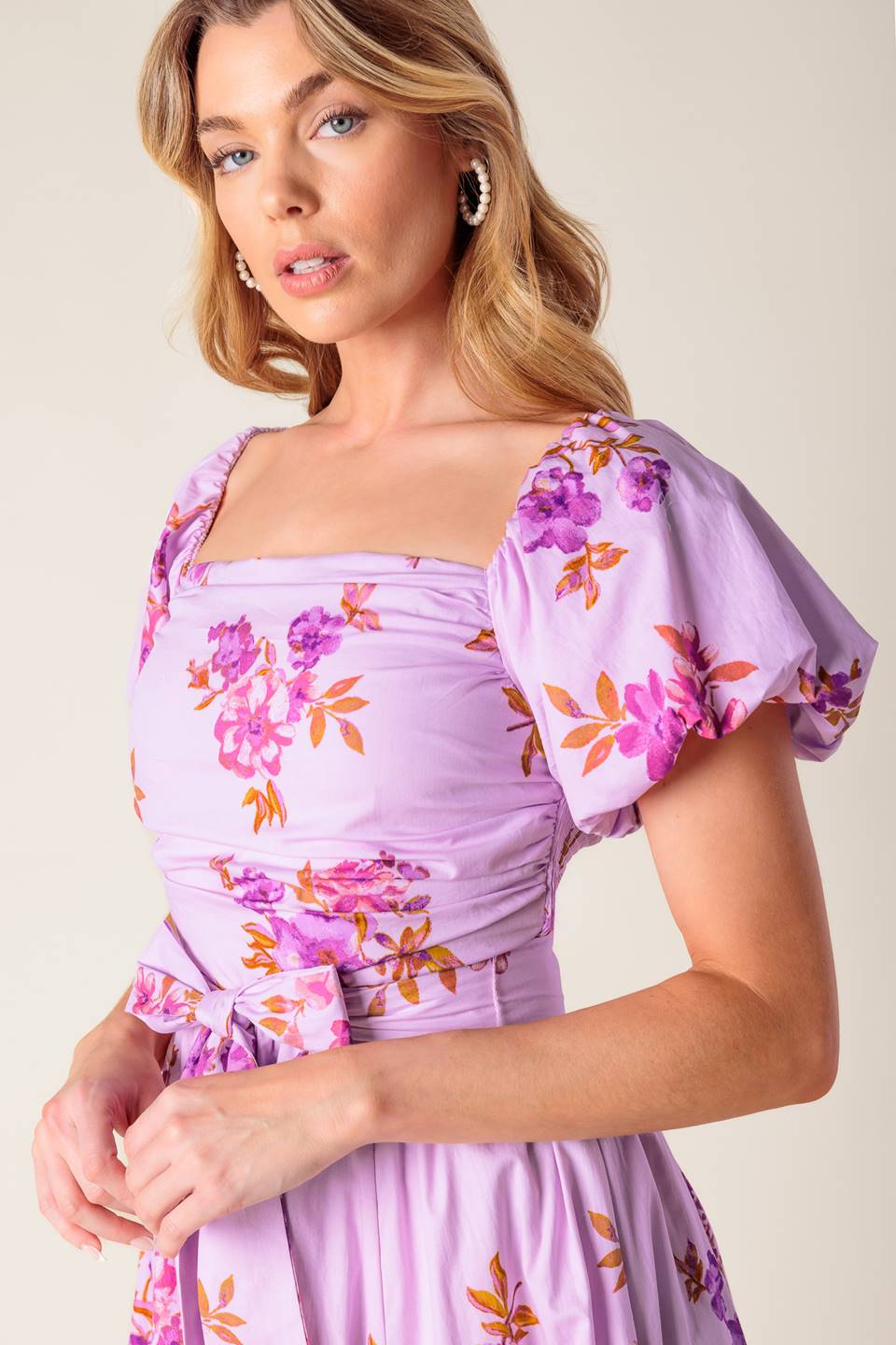 A lavender printed woven midi dress featuring on/off shoulder neckline, shirred bodice, self sash tie, full skirt and smocked back bodice.