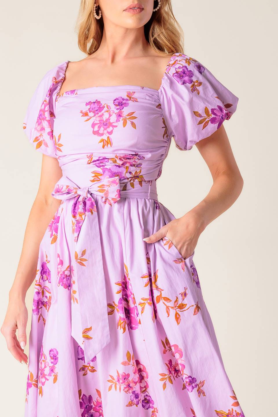 A lavender printed woven midi dress featuring on/off shoulder neckline, shirred bodice, self sash tie, full skirt and smocked back bodice.