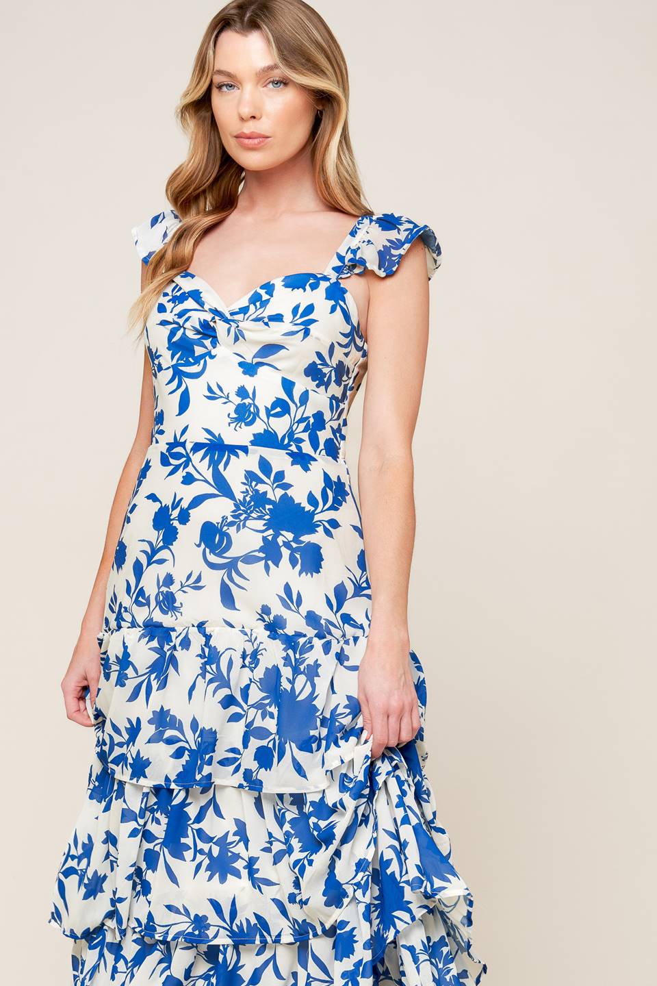 A printed woven maxi dress featuring sweetheart neckline with twist bodice, ruffled sleeve, waist yoke, layered skirt and back zipper closure.