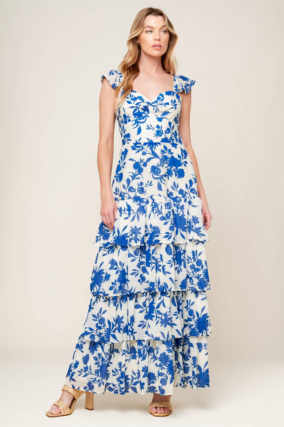 A printed woven maxi dress featuring sweetheart neckline with twist bodice, ruffled sleeve, waist yoke, layered skirt and back zipper closure.