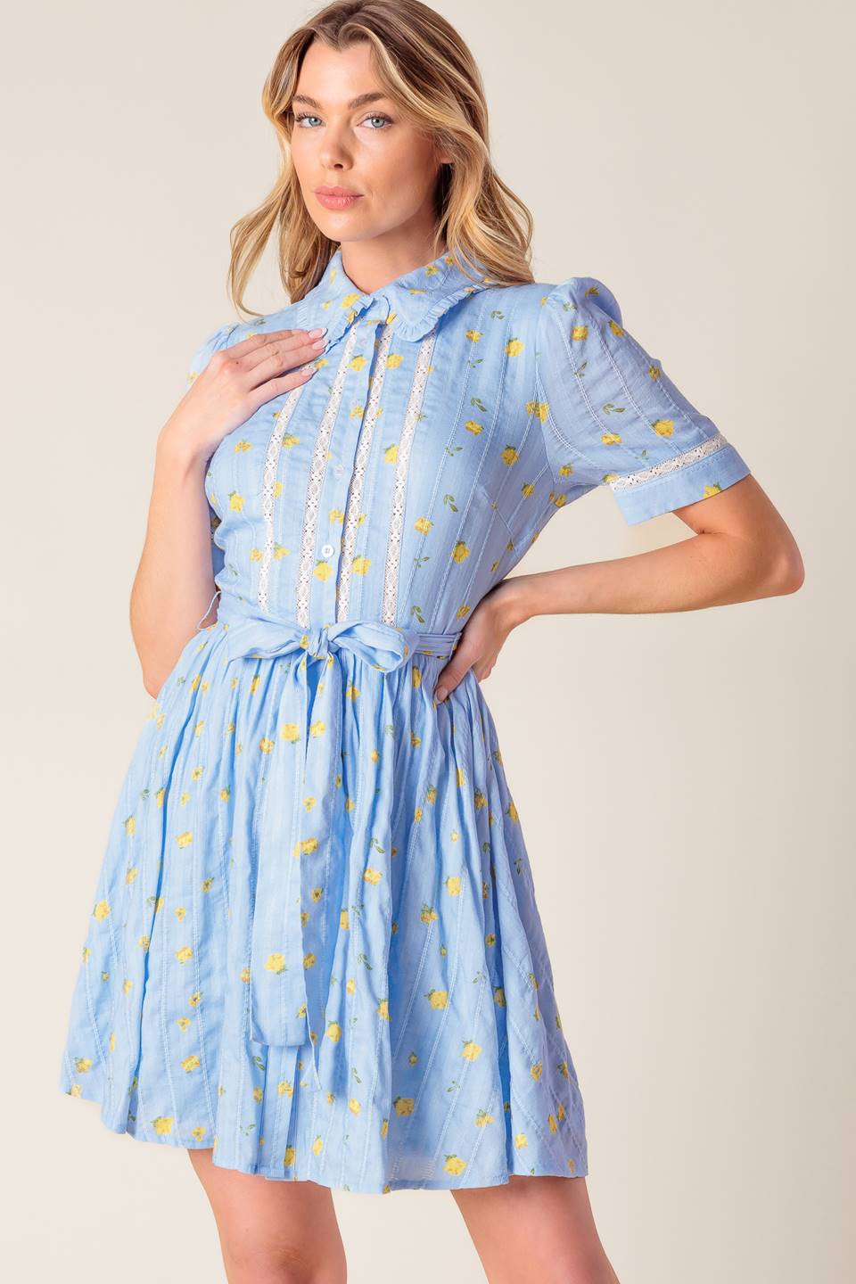 A blue printed woven mini dress featuring collar, button down, short sleeve, lace inset, self sash and full skirt.