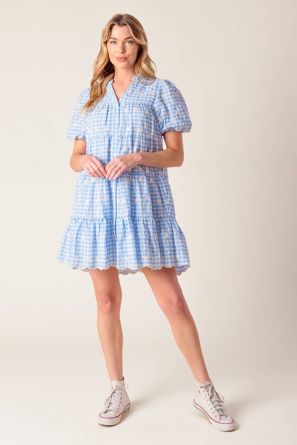 A woven powder blue gingham babydoll dress featuring V neckline, short puff sleeve and tiered body with ruffled hemline.