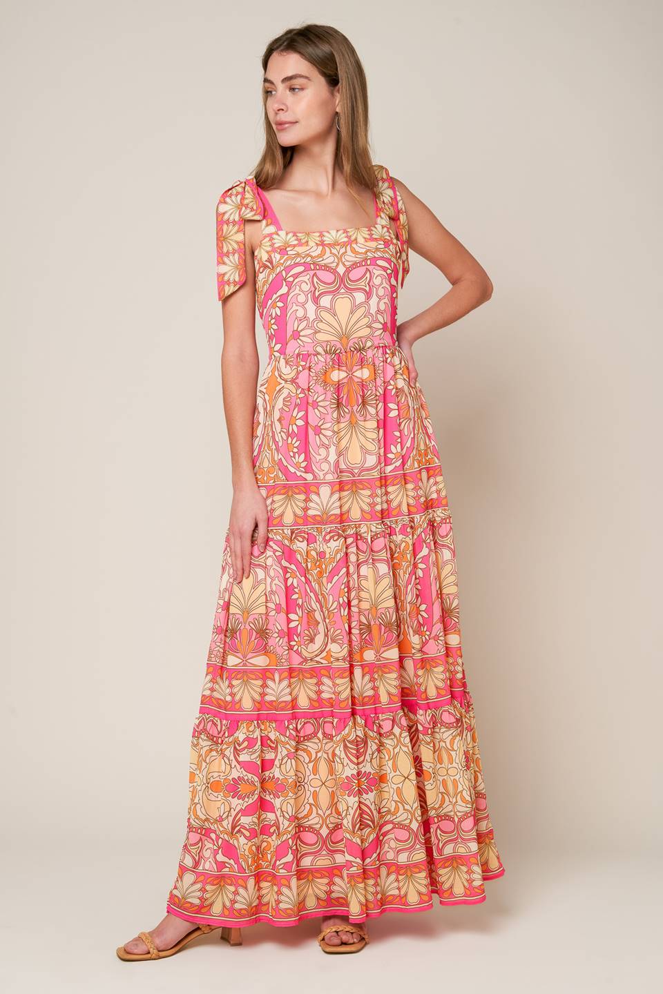 This woven maxi dress showcases a printed design, along with a straight neckline, shoulder tie, tiered skirt, and a back zipper closure.