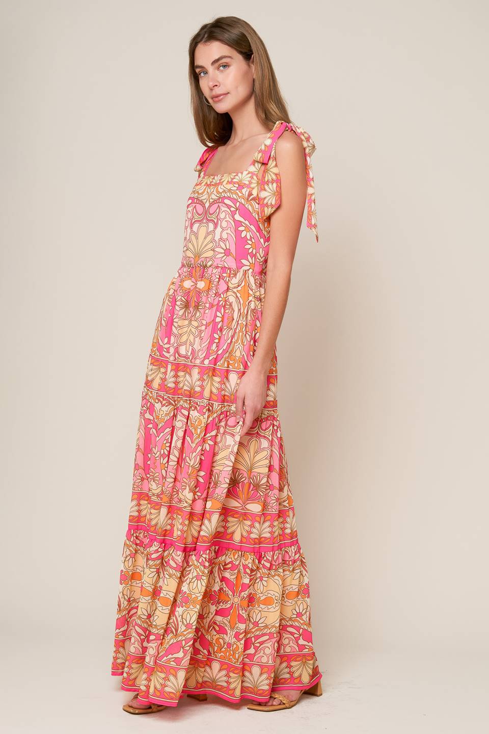 This woven maxi dress showcases a printed design, along with a straight neckline, shoulder tie, tiered skirt, and a back zipper closure.