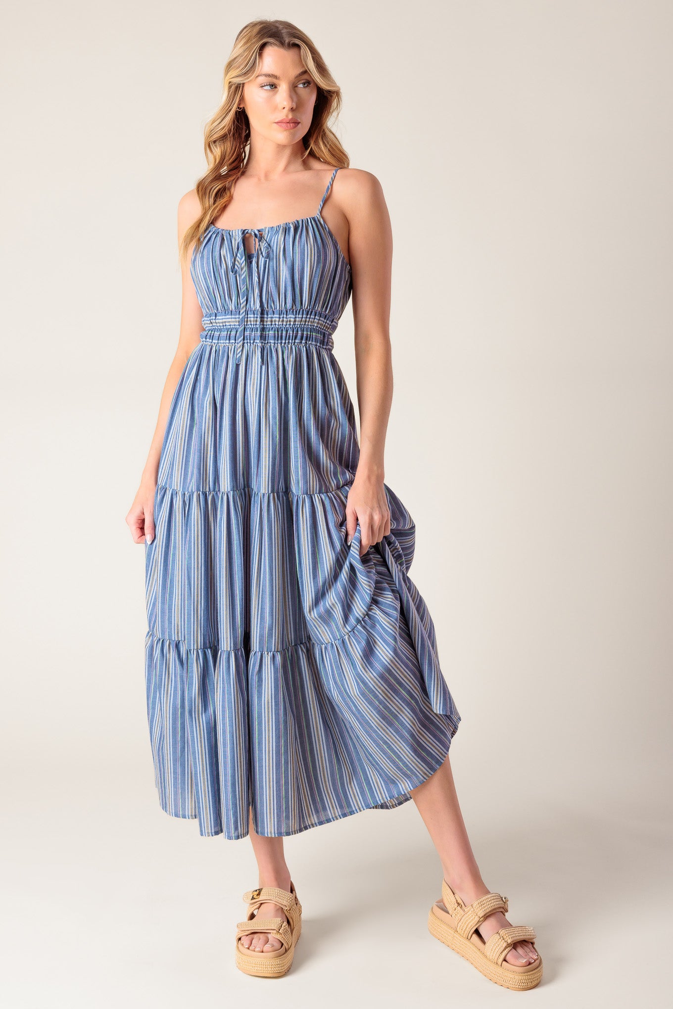 A blue striped woven midi dress featuring straight neckline with front tie, elasticized waist and tiered skirt.