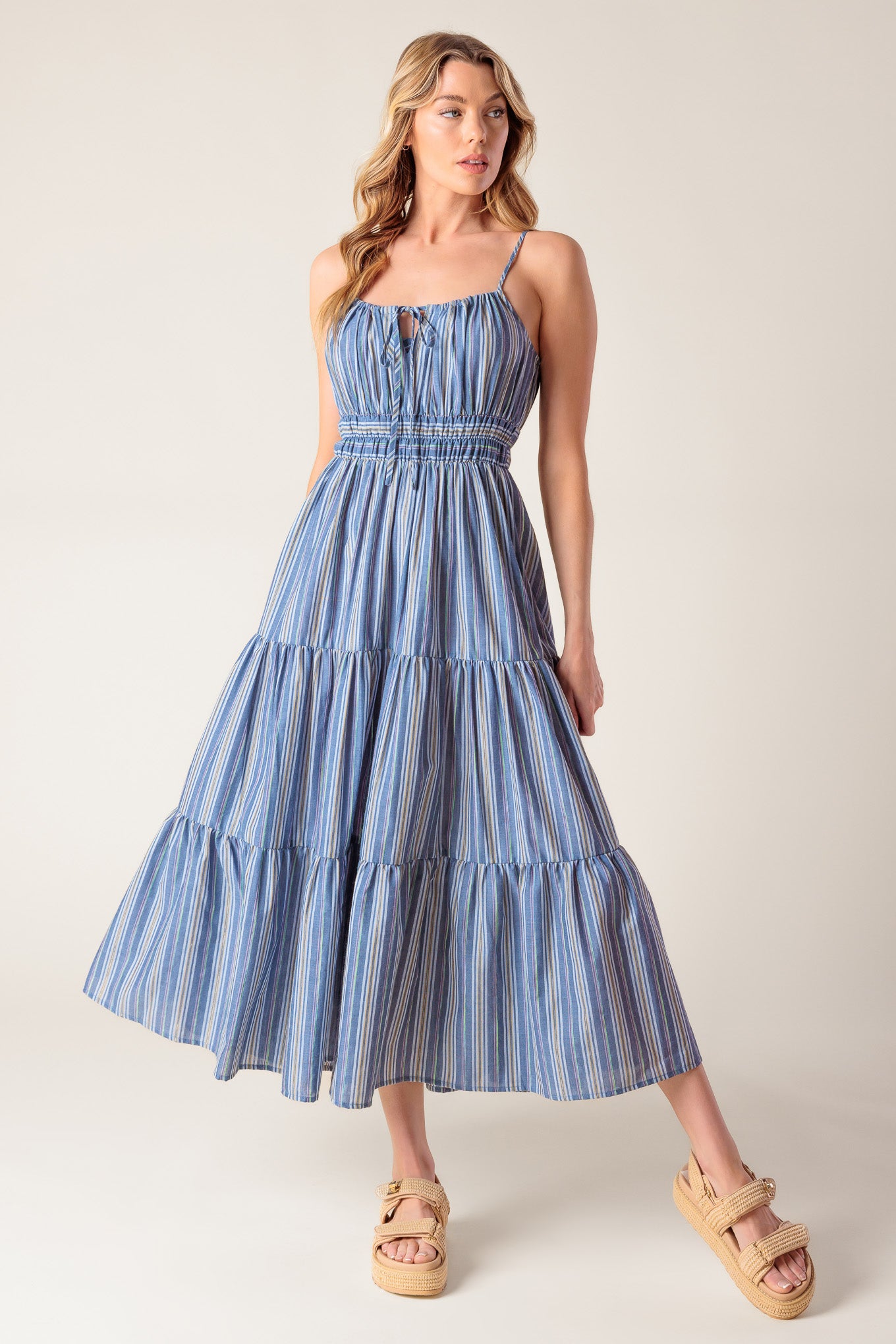 A blue striped woven midi dress featuring straight neckline with front tie, elasticized waist and tiered skirt.