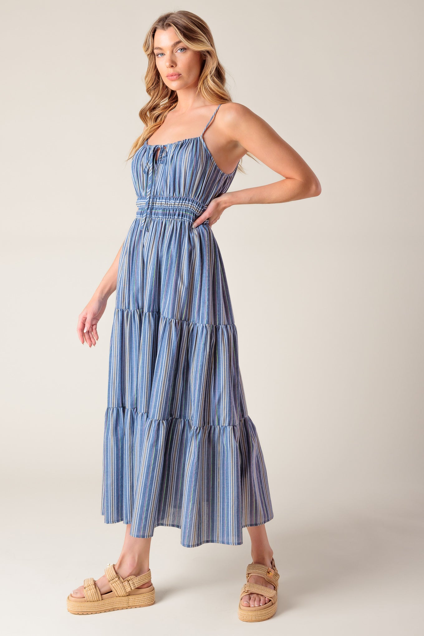 A blue striped woven midi dress featuring straight neckline with front tie, elasticized waist and tiered skirt.