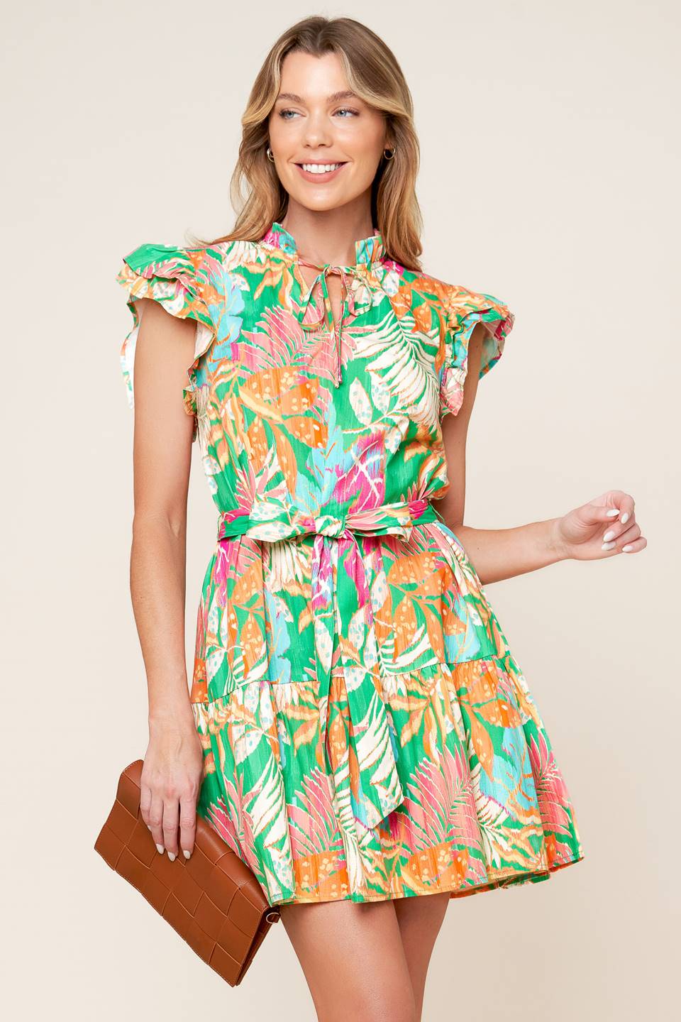 A printed woven mini dress featuring high neckline ruffled edge with front tie, double ruffled sleeve, self sash tie and ruffled hemline.