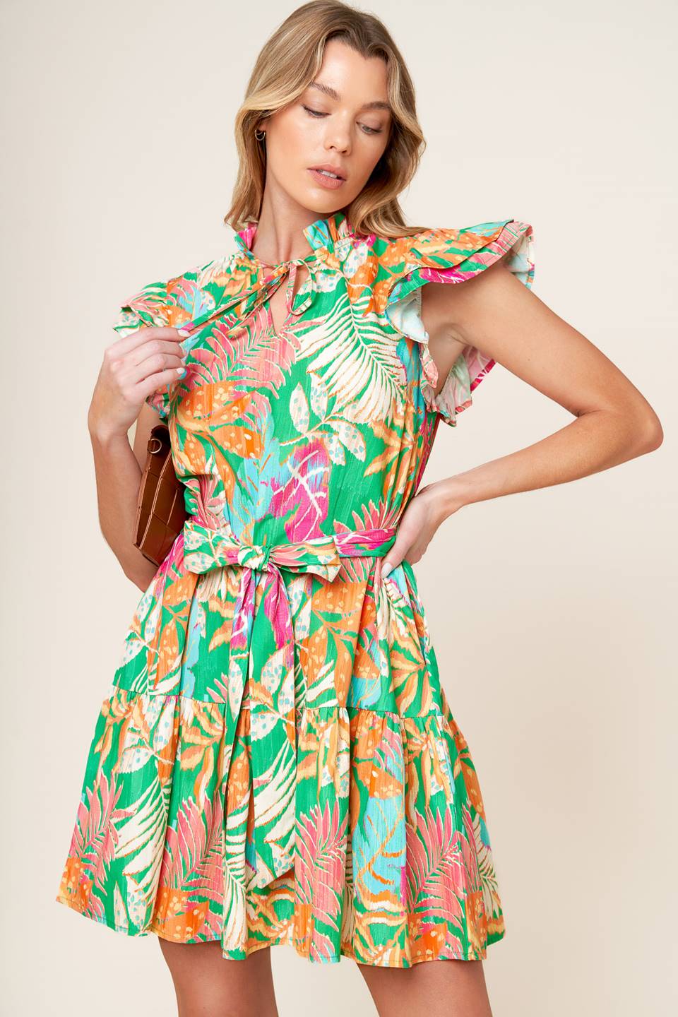 A printed woven mini dress featuring high neckline ruffled edge with front tie, double ruffled sleeve, self sash tie and ruffled hemline.