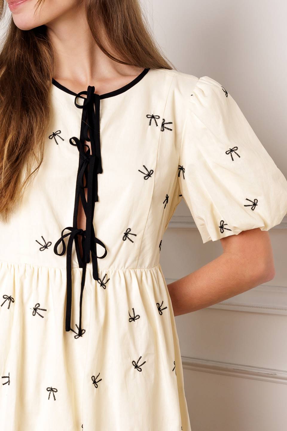 A perfect addition to your wardrobe, this solid embroidered mini dress is designed with a round neckline and adorable front bow ties, accompanied by short puff sleeves.