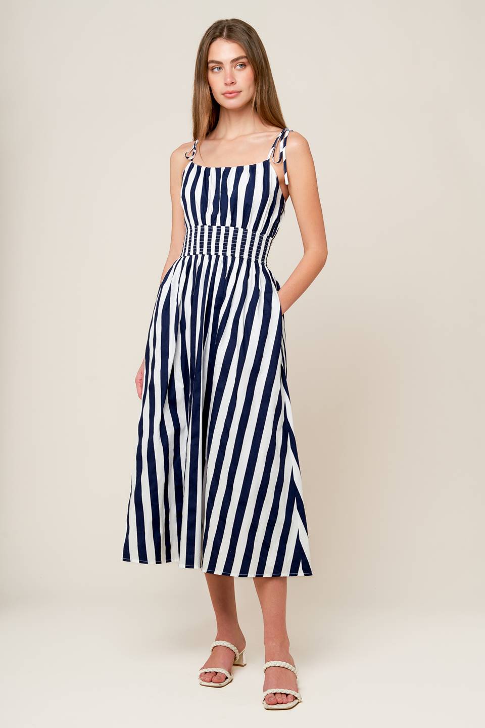 A white and navy striped printed woven midi dress featuring tank bodice with shoulder strap, wide smocked waistband and full skirt.