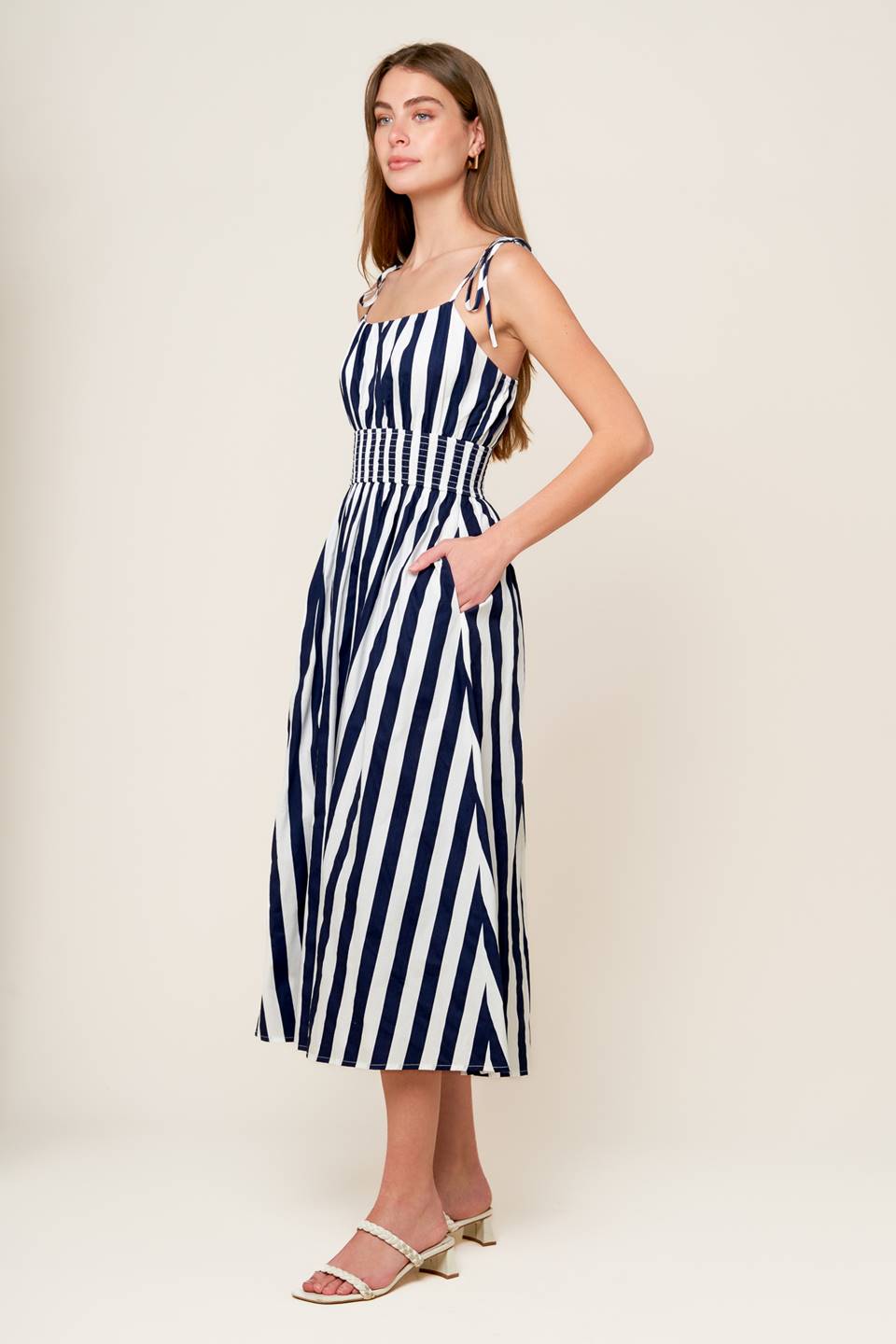 A white and navy striped printed woven midi dress featuring tank bodice with shoulder strap, wide smocked waistband and full skirt.