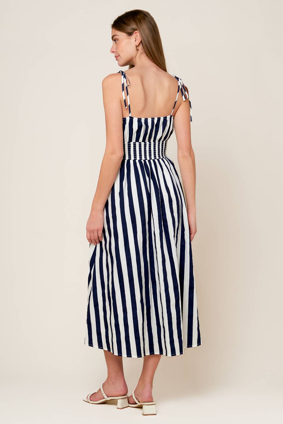 A white and navy striped printed woven midi dress featuring tank bodice with shoulder strap, wide smocked waistband and full skirt.