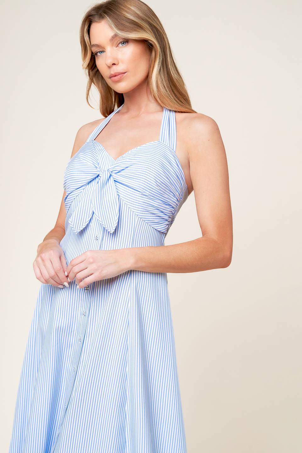 A striped woven midi dress featuring halter neckline, front tie, button down detail and back zipper closure