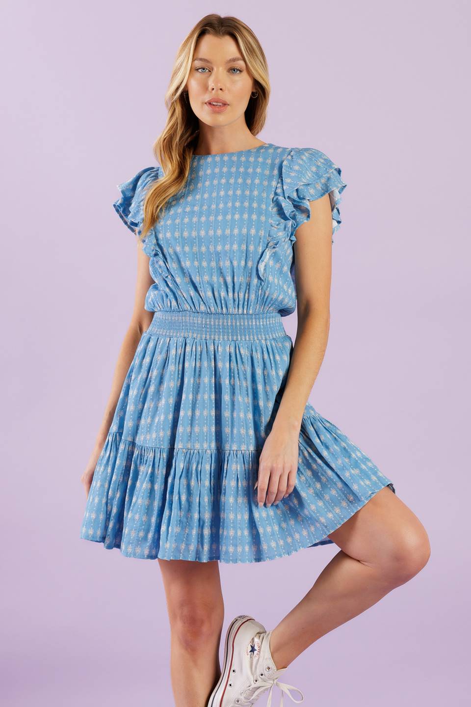 A textured woven mini dress featuring round neckline, ruffled short sleeve, smocked waistband, ruffled hemline and back neck button closure