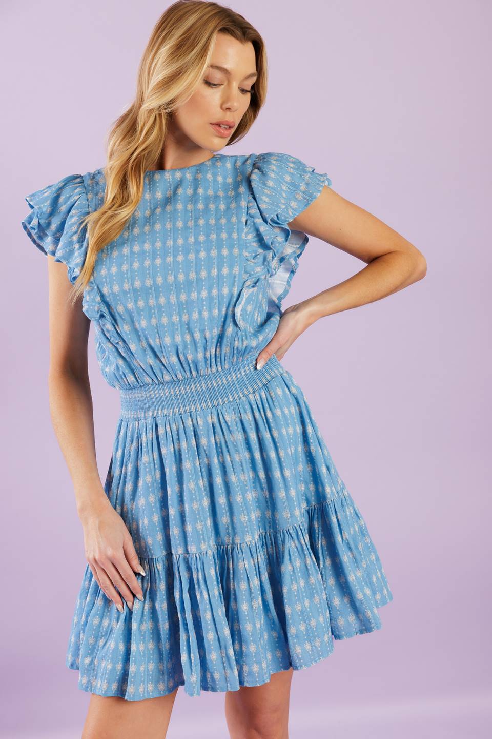 A textured woven mini dress featuring round neckline, ruffled short sleeve, smocked waistband, ruffled hemline and back neck button closure