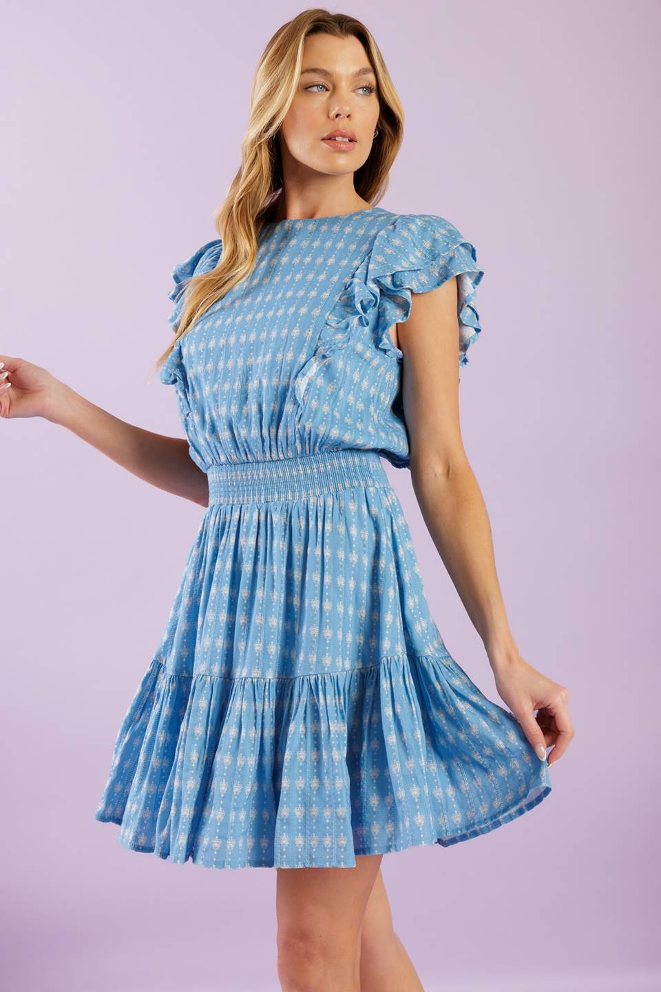 A textured woven mini dress featuring round neckline, ruffled short sleeve, smocked waistband, ruffled hemline and back neck button closure