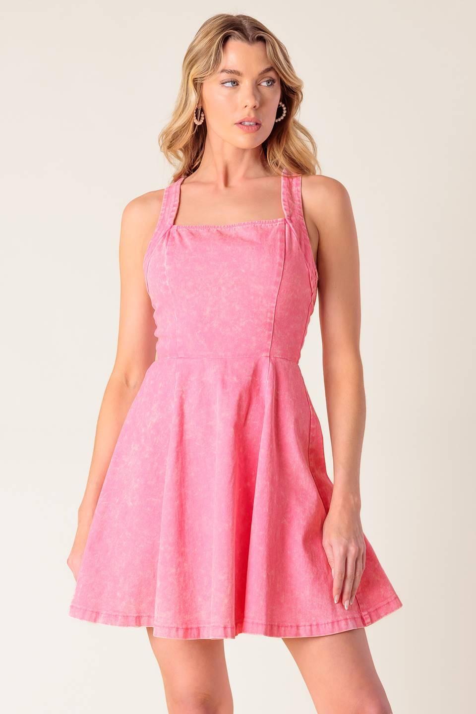 A pink acid washed woven mini dress featuring halter neckline, full skirt bare back with criss cross strap and zipper closure.