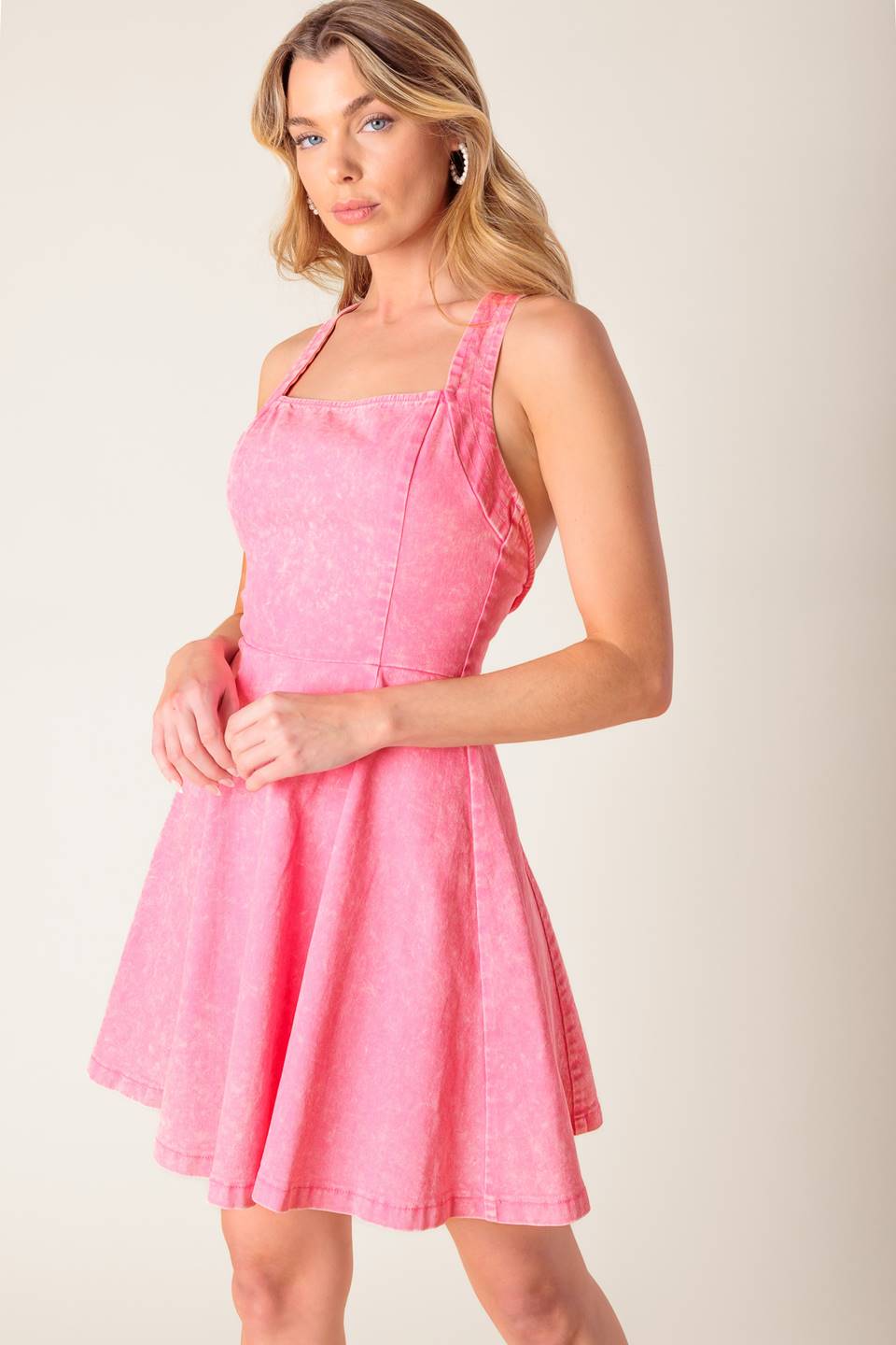 A pink acid washed woven mini dress featuring halter neckline, full skirt bare back with criss cross strap and zipper closure.