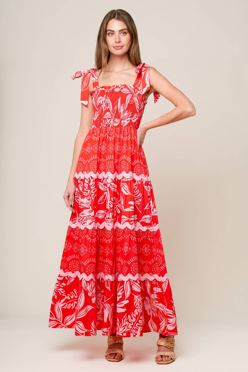 A red and pink printed woven maxi dress featuring straight neckline with ruffled edge, shoulder ties, smocked bodice and tiered skirt with ric-rac ribbon inset.