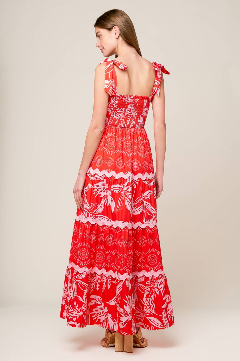 A red and pink printed woven maxi dress featuring straight neckline with ruffled edge, shoulder ties, smocked bodice and tiered skirt with ric-rac ribbon inset.