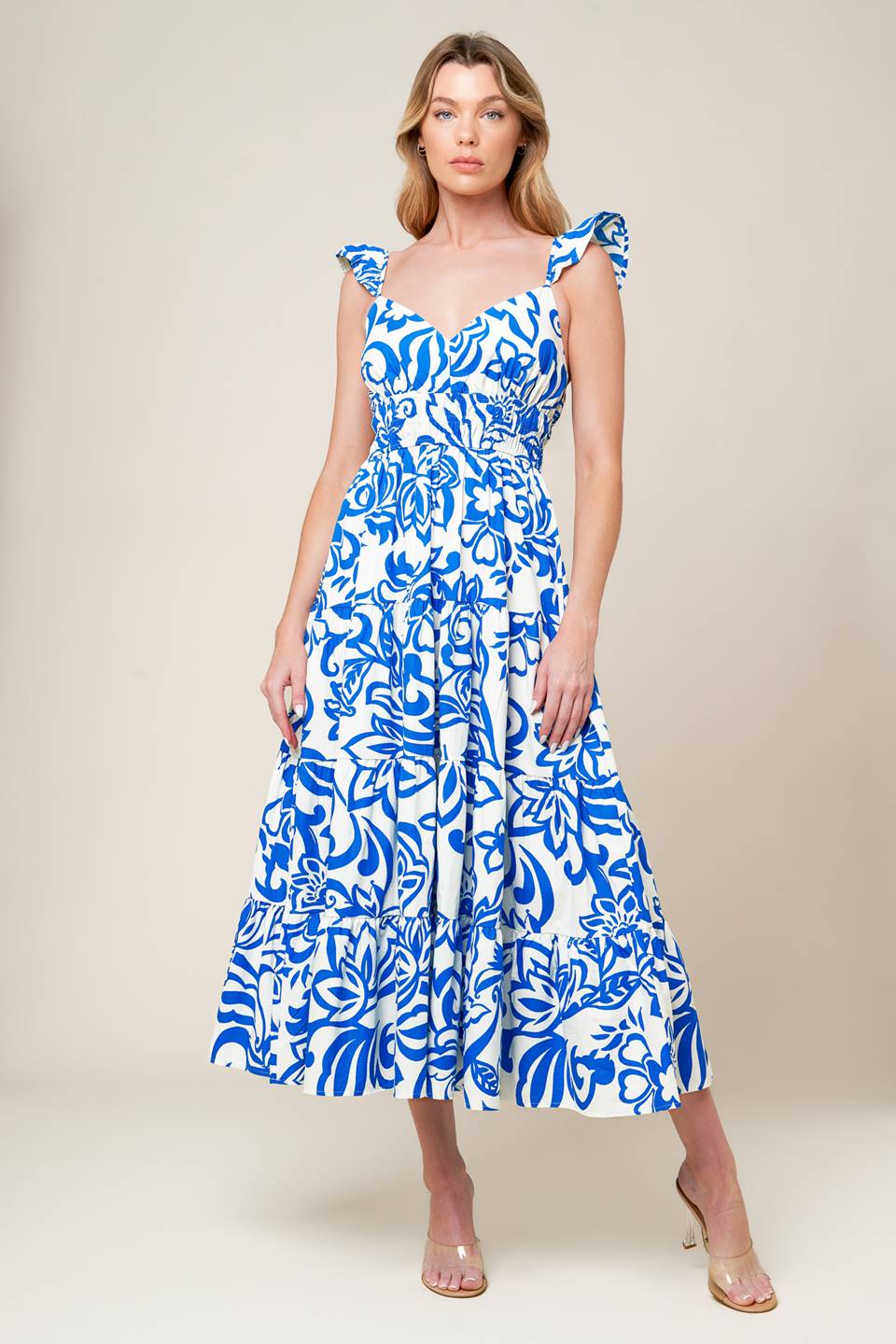 A blue and white printed woven midi dress featuring cami top with ruffle sleeve, elasticized wide waistband and tiered skirt.