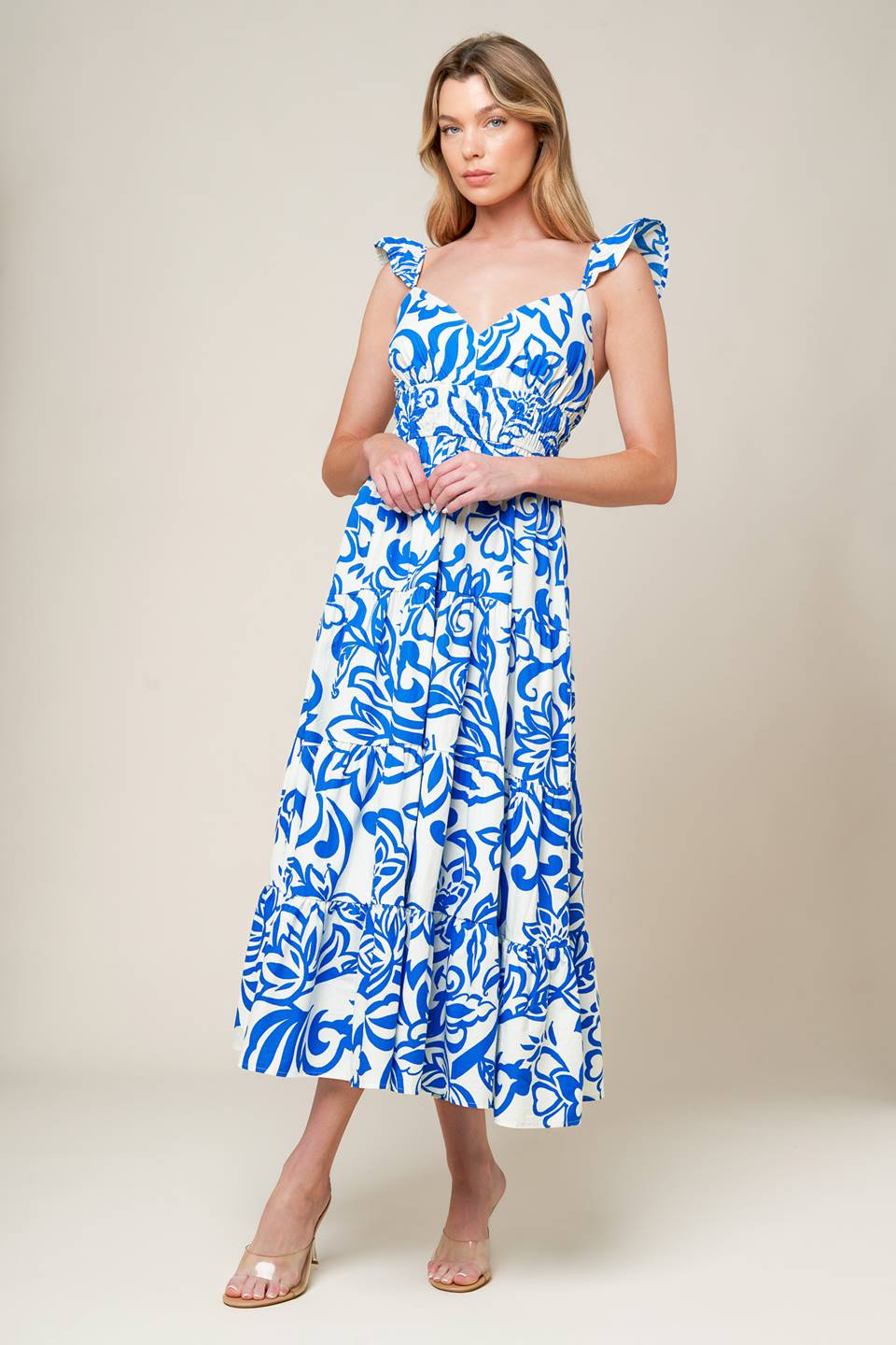 A blue and white printed woven midi dress featuring cami top with ruffle sleeve, elasticized wide waistband and tiered skirt.