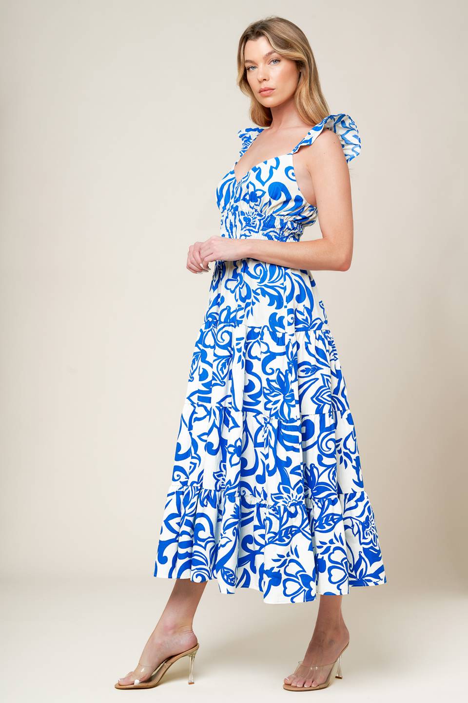 A blue and white printed woven midi dress featuring cami top with ruffle sleeve, elasticized wide waistband and tiered skirt.