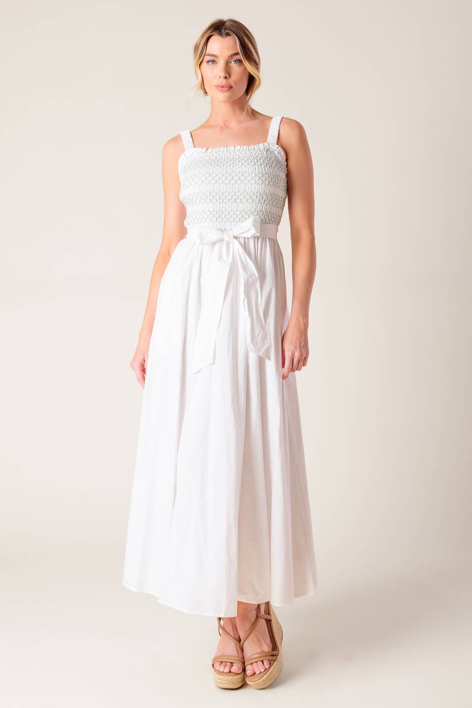 A solid white woven midi dress featuring straight neckline, straps, color smocked bodice and full skirt.