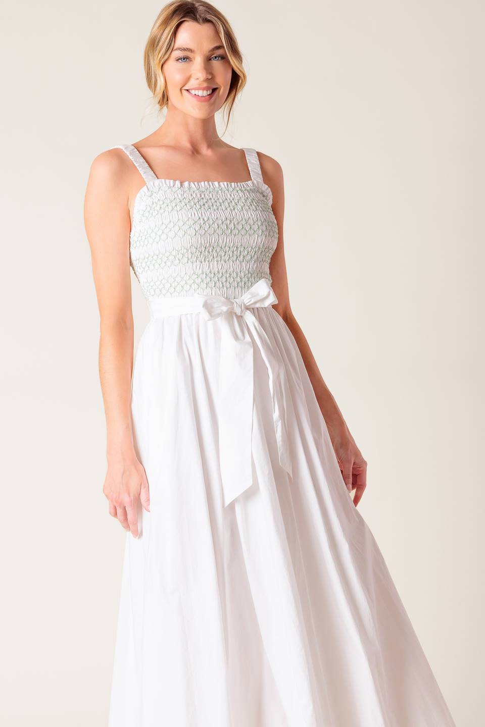 A solid white woven midi dress featuring straight neckline, straps, color smocked bodice and full skirt.