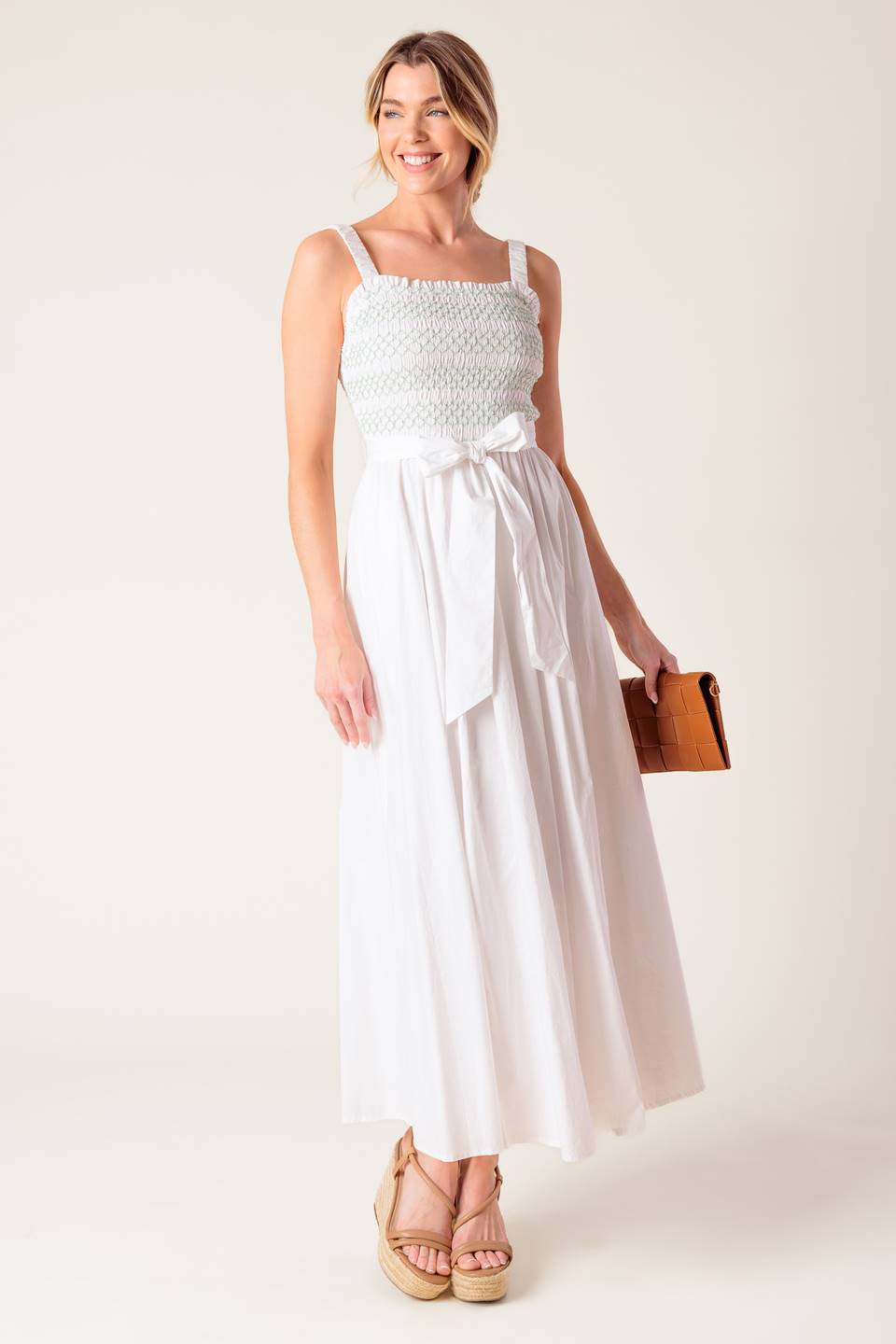 A solid white woven midi dress featuring straight neckline, straps, color smocked bodice and full skirt.