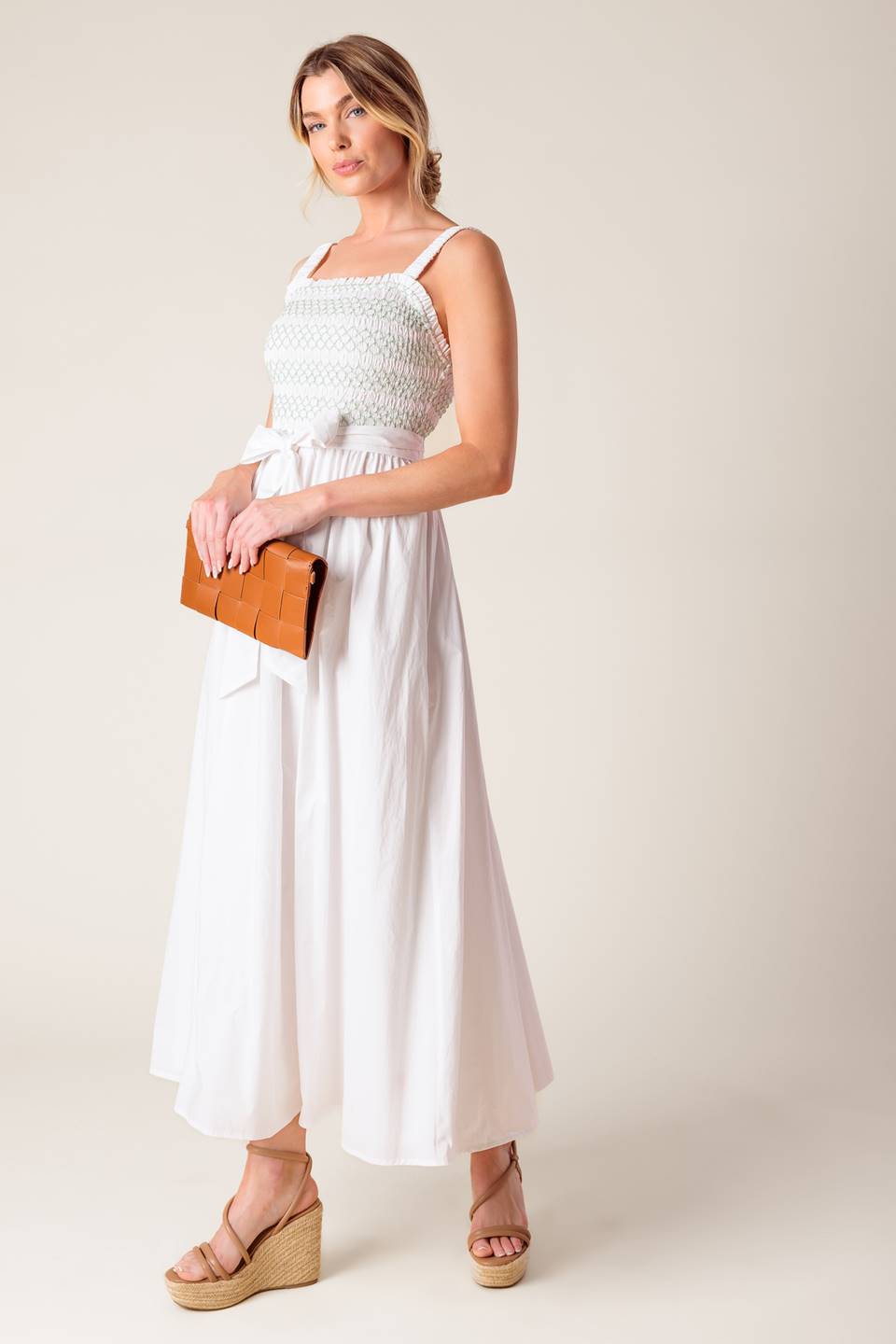 A solid white woven midi dress featuring straight neckline, straps, color smocked bodice and full skirt.