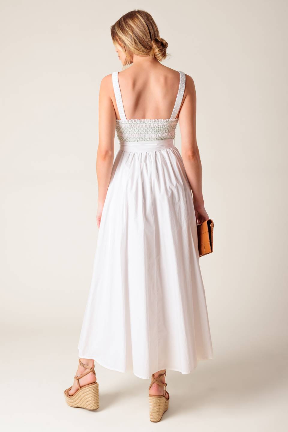 A solid white woven midi dress featuring straight neckline, straps, color smocked bodice and full skirt.