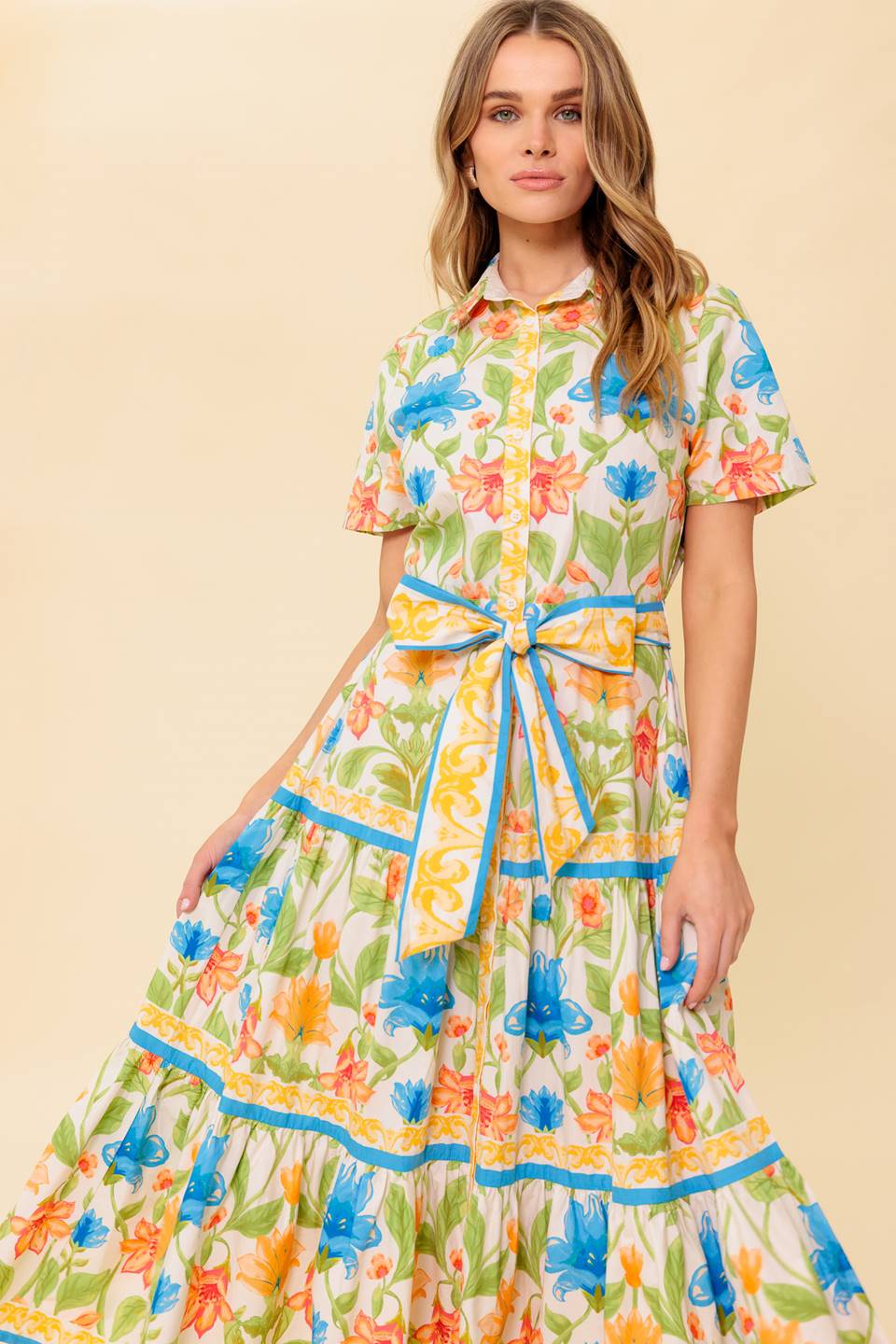 A printed woven midi dress featuring shirt collar, short sleeve, button down, self sash tie and tiered skirt