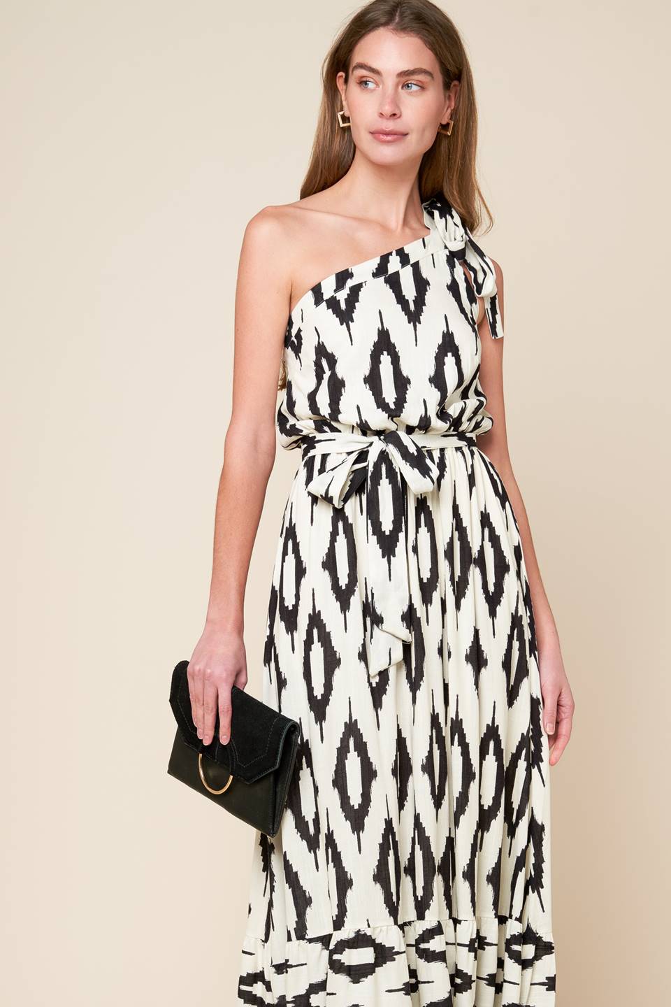 A printed woven maxi dress featuring one shoulder neckline with tie, elasticized waist with self sash tie and ruffled hemline.