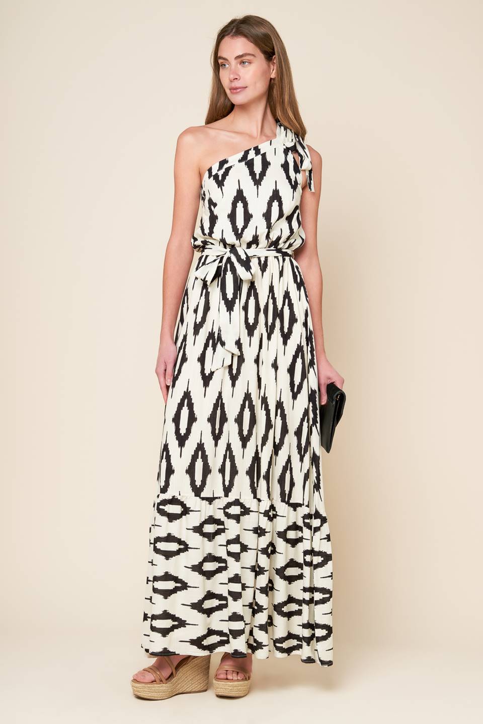 A printed woven maxi dress featuring one shoulder neckline with tie, elasticized waist with self sash tie and ruffled hemline.