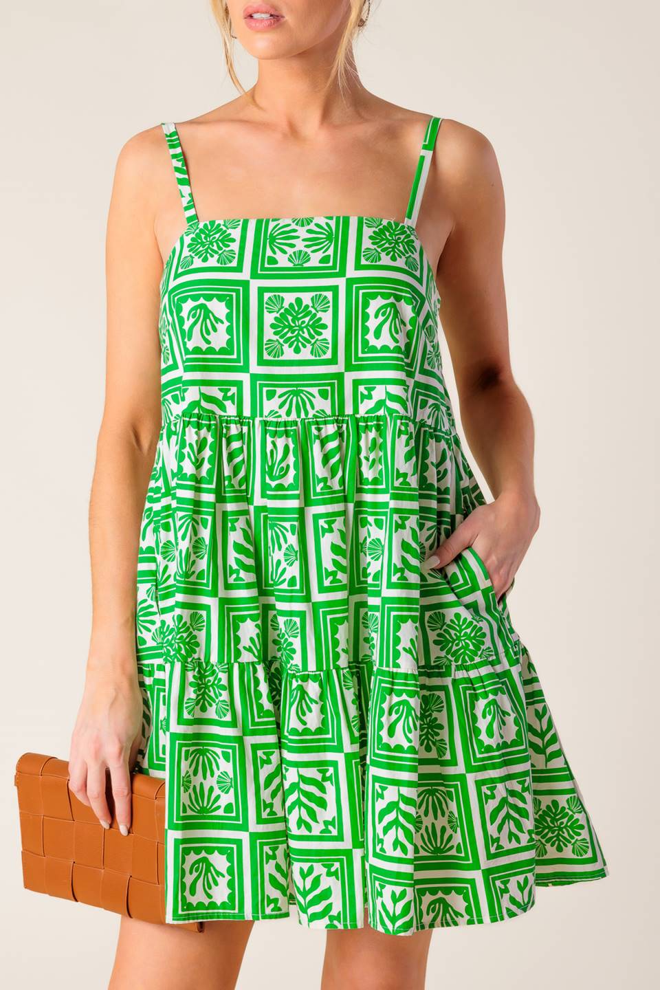 A white and green printed woven mini dress featuring straight neckline, straps and tiered body