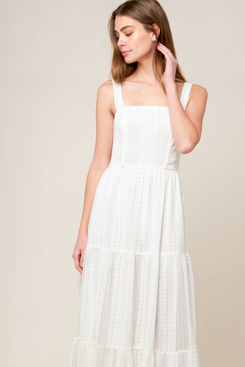 A white woven lace maxi dress featuring straight neckline, straps, tiered skirt and back zipper closure.