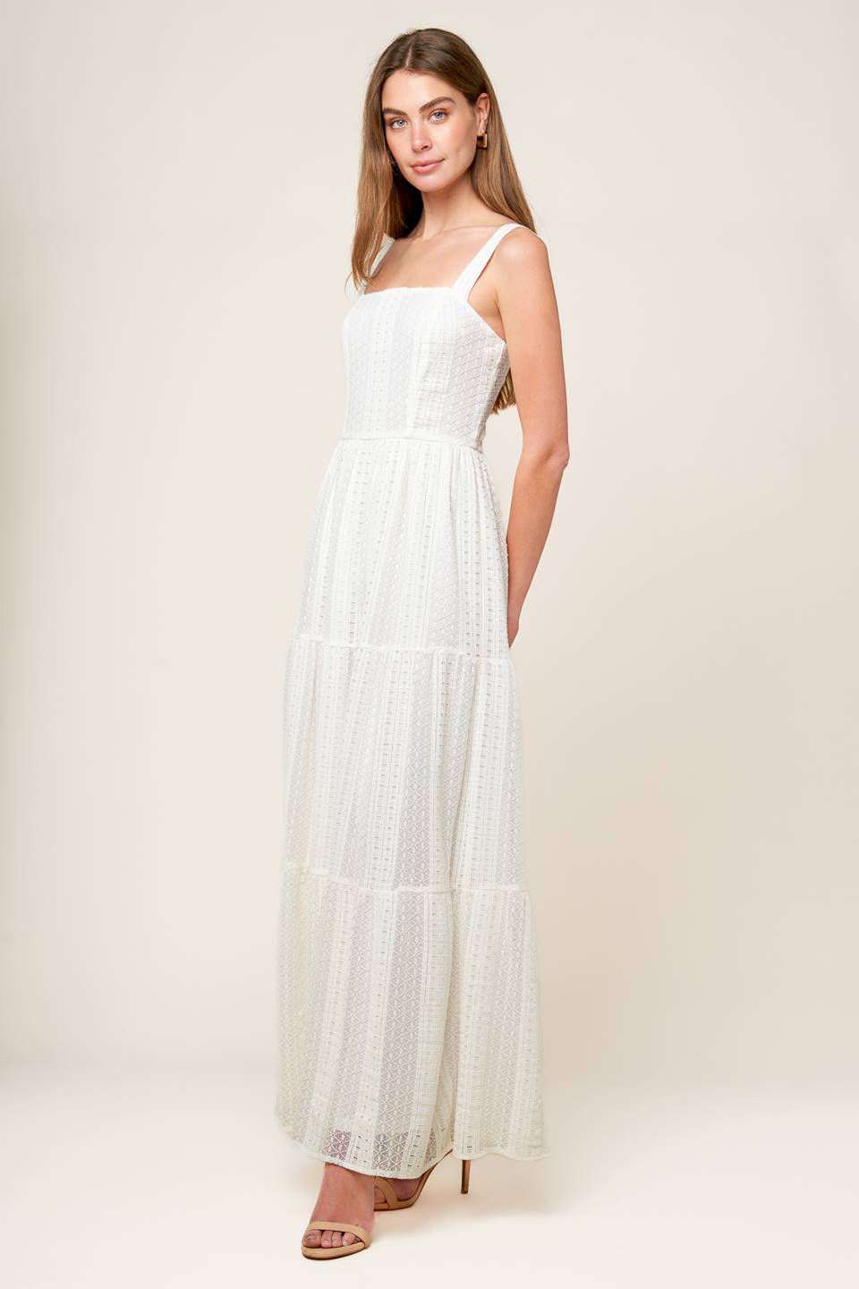 A white woven lace maxi dress featuring straight neckline, straps, tiered skirt and back zipper closure.