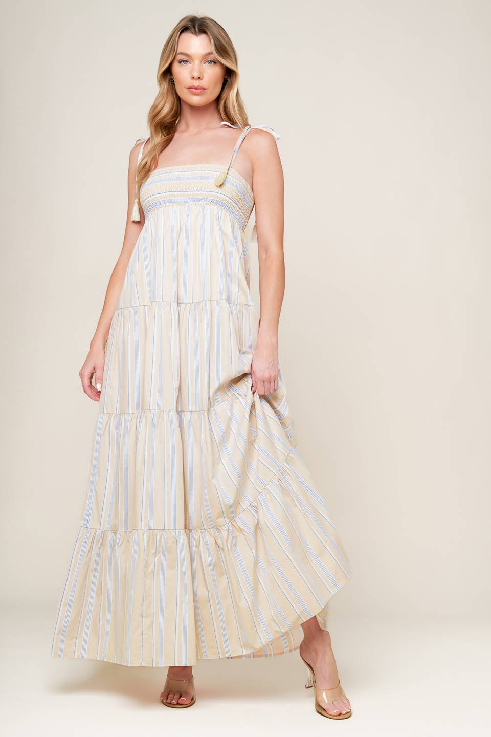 A striped woven maxi dress featuring smocked bodice, shoulder straps with tassel and tiered skirt.