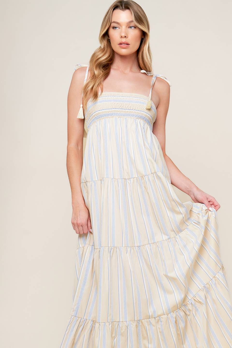 A striped woven maxi dress featuring smocked bodice, shoulder straps with tassel and tiered skirt.