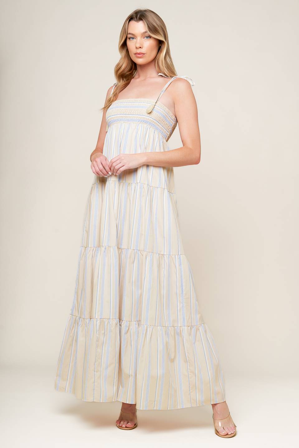 A striped woven maxi dress featuring smocked bodice, shoulder straps with tassel and tiered skirt.