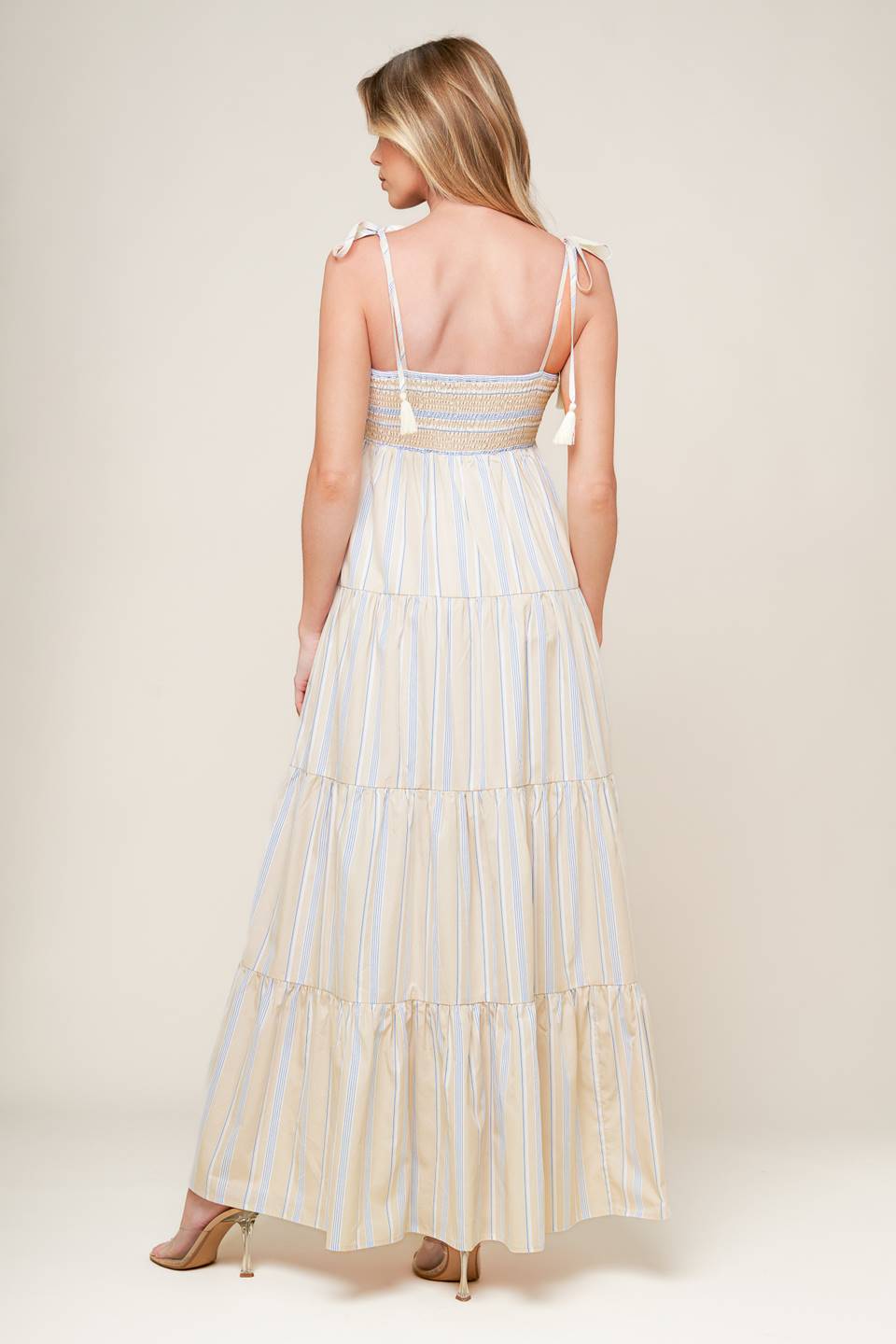 A striped woven maxi dress featuring smocked bodice, shoulder straps with tassel and tiered skirt.