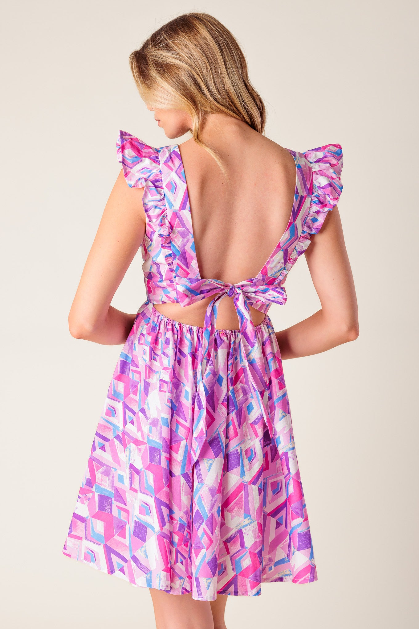 A pink and blue printed woven mini dress featuring V neckline, ruffled sleeve, waist yoke, full skirt, bare back with tie closure.