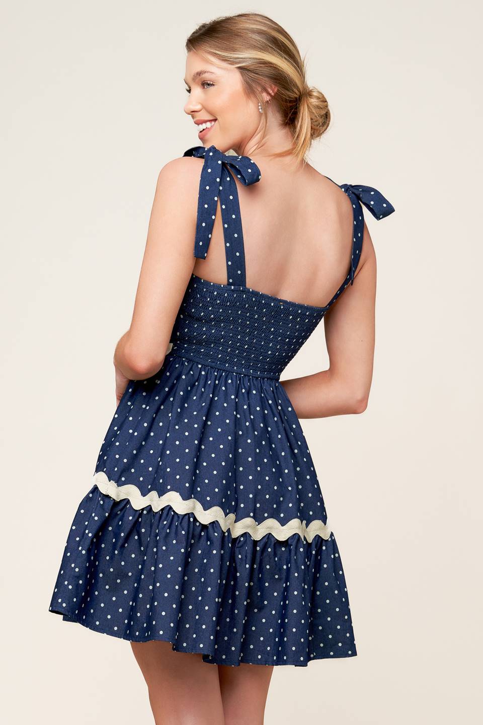 A dotted woven mini dress featuring straight neckline, ric rac ribbon detail, shoulder ties and smocked back bodice.