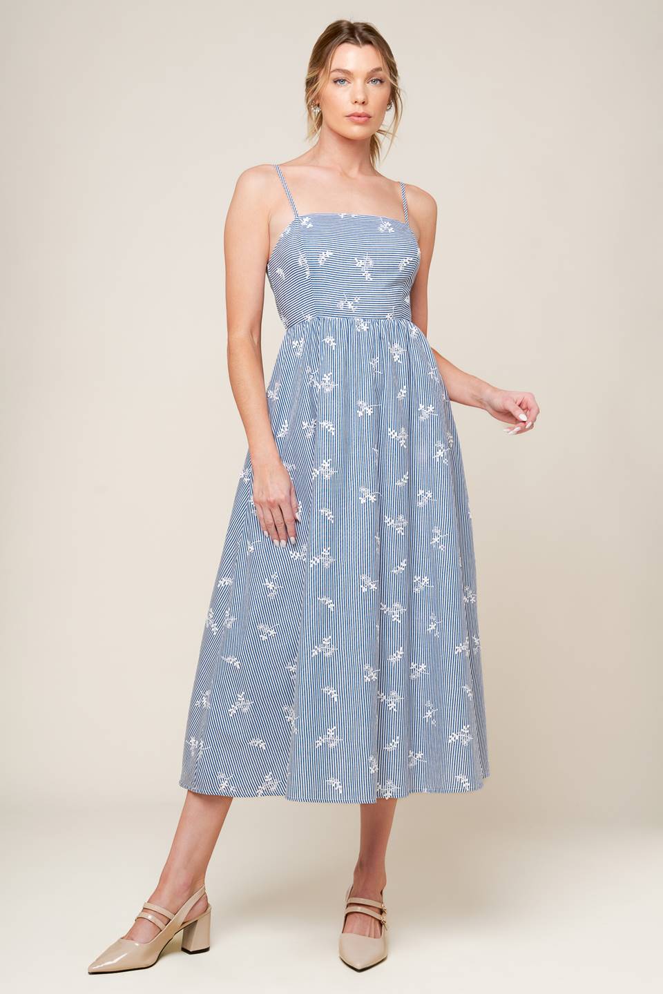 A blue and white striped woven midi dress featuring straight neckline, straps, full skirt, bare back with tie detail featuring white embroidery.