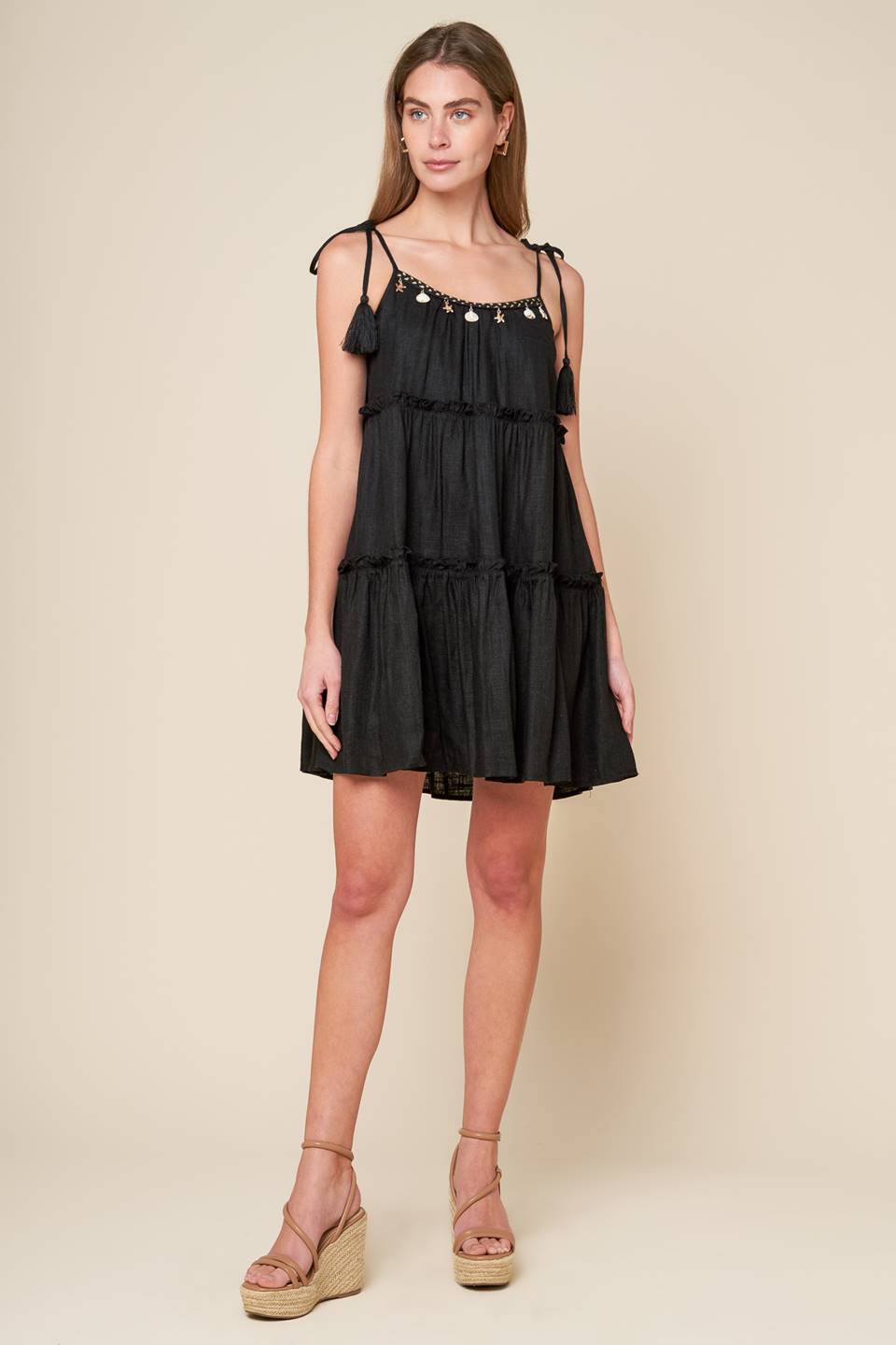 A black solid woven mini dress featuring U neckline, shoulder tie with tassel, seashell trim and tiered body.