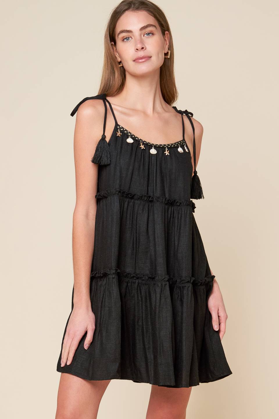 A black solid woven mini dress featuring U neckline, shoulder tie with tassel, seashell trim and tiered body.