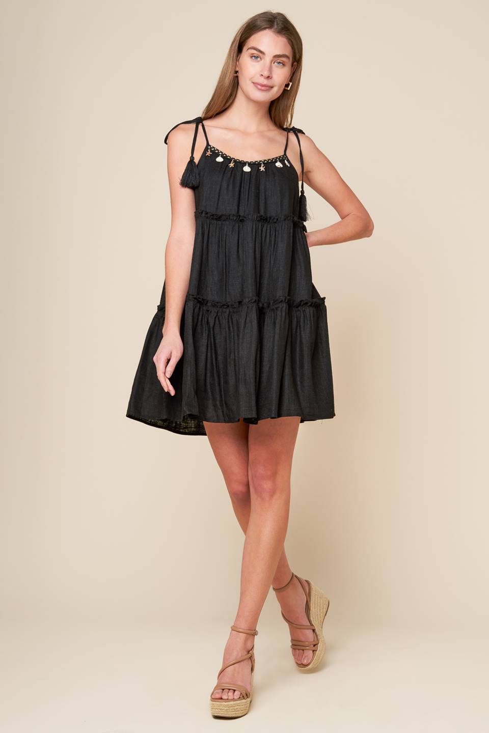 A black solid woven mini dress featuring U neckline, shoulder tie with tassel, seashell trim and tiered body.