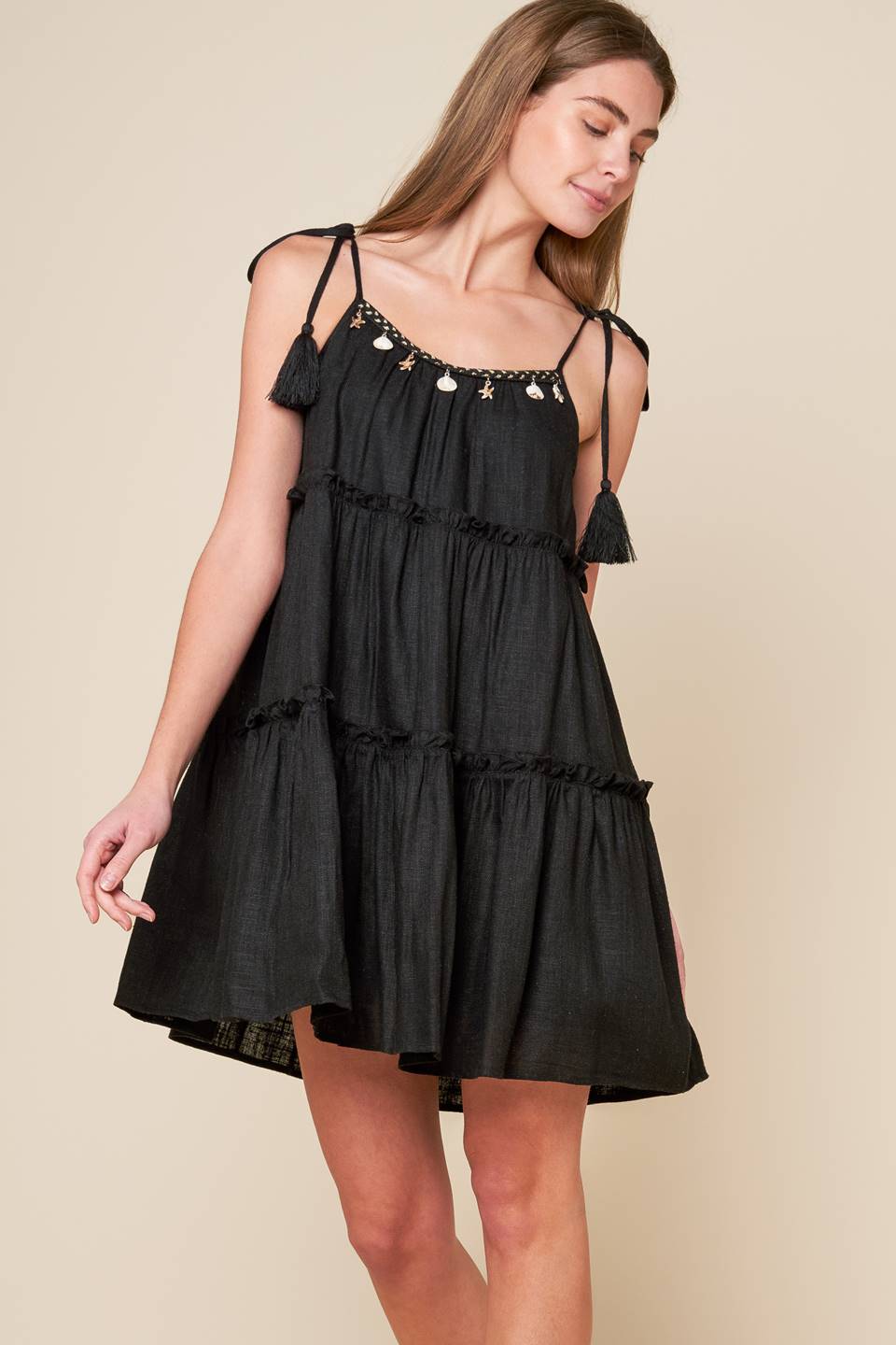 A black solid woven mini dress featuring U neckline, shoulder tie with tassel, seashell trim and tiered body.